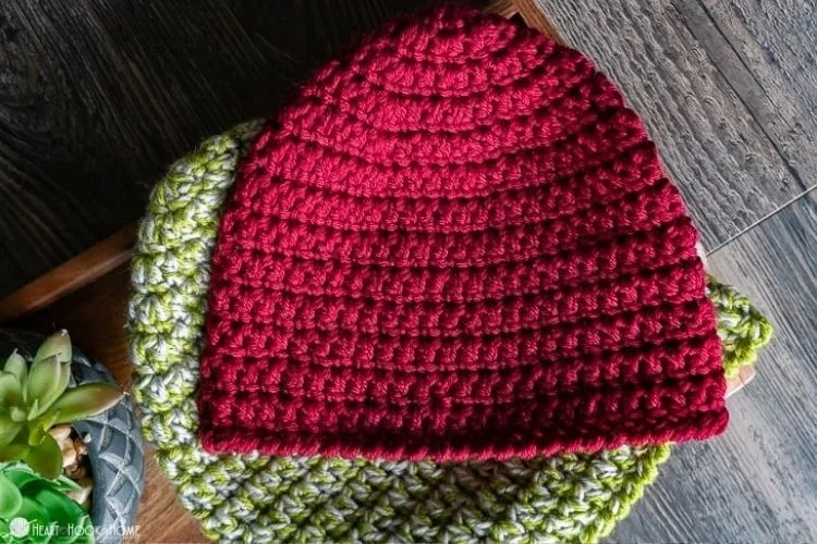 A red and green crocheted beanie on a wooden table.