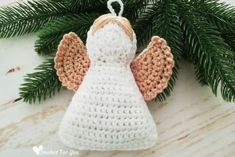 A white crocheted angel ornament hanging on a pine tree.