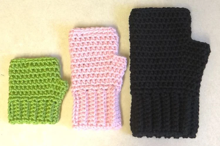 Three crocheted fingerless mitts on a white surface.