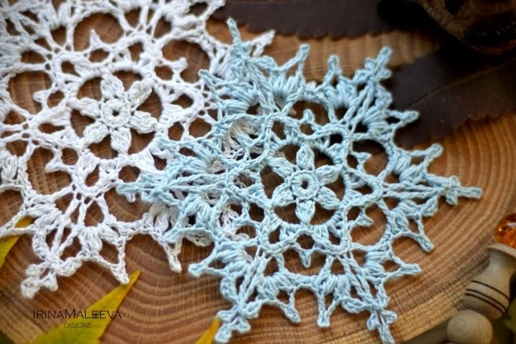 Two crocheted snowflakes on a piece of wood.