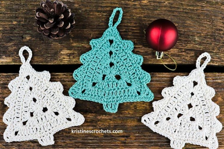 Three crocheted Christmas tree ornaments on a wooden table.