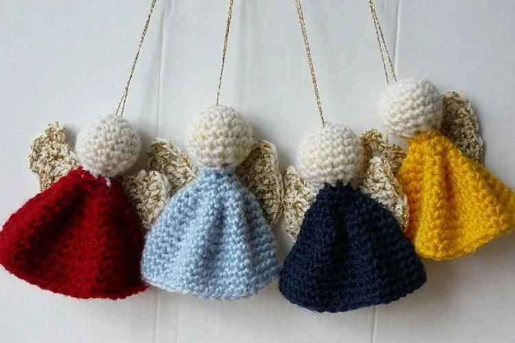 Four crocheted angel ornaments hanging on a white wall.