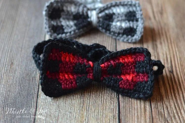 Two crocheted bow ties on a wooden table.