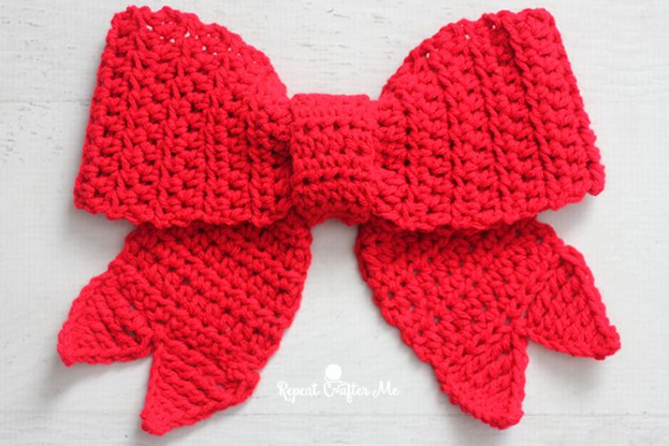 A red crocheted bow on a white surface.