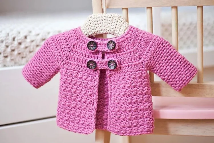 A pink crocheted jacket hanging on a chair.