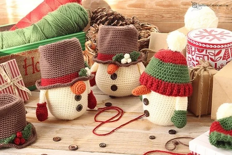 Four crocheted snowmen sitting on a wooden table.