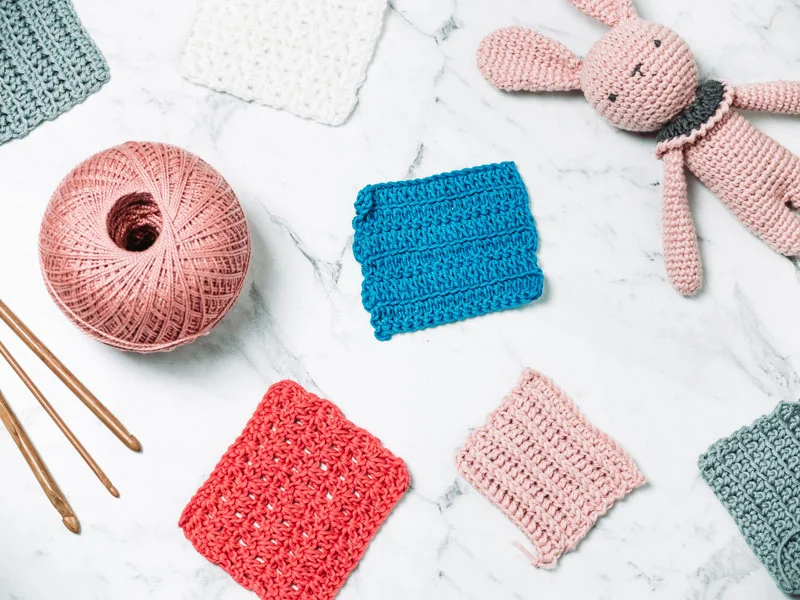 A crocheted bunny, yarn and crochet needles on a marble table.