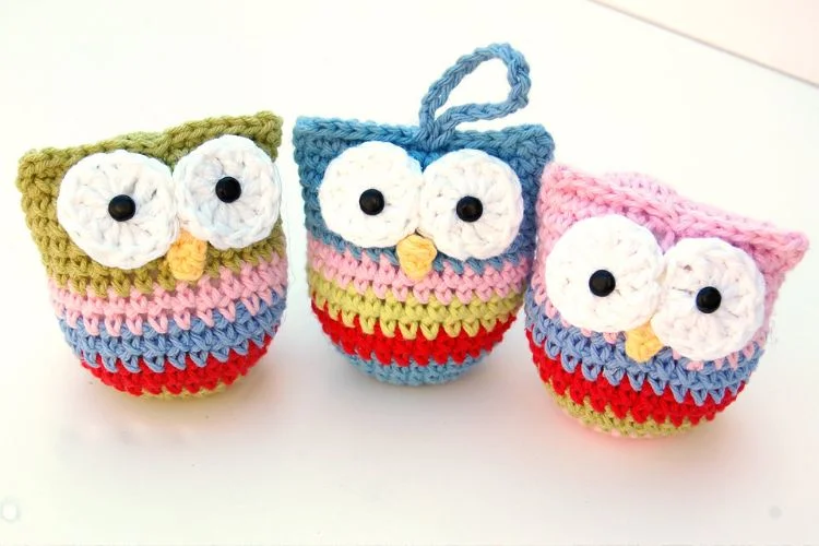 Three crocheted owls on a white surface.