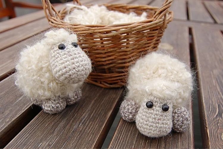 Two crocheted sheep sitting next to a basket.