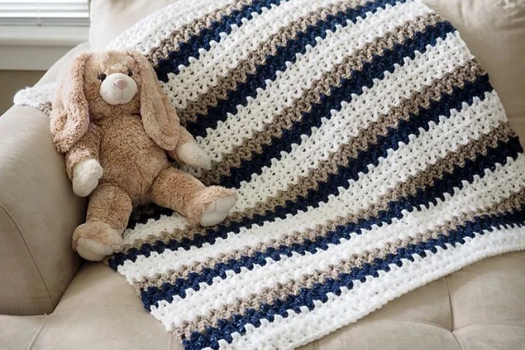 A teddy bear sits on a couch with a crocheted blanket.