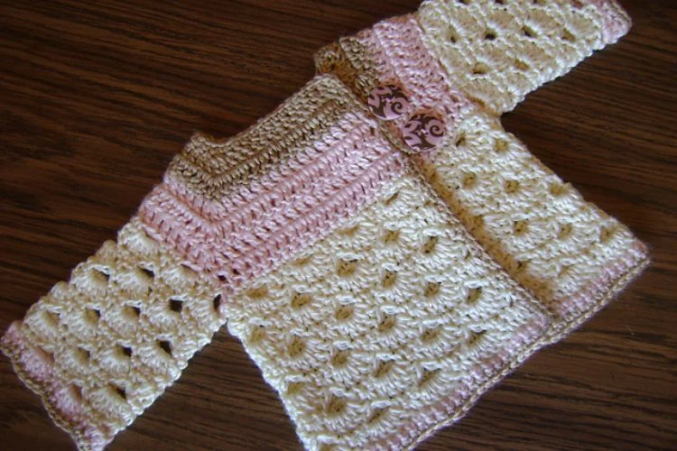 A crocheted baby jacket on a wooden table.