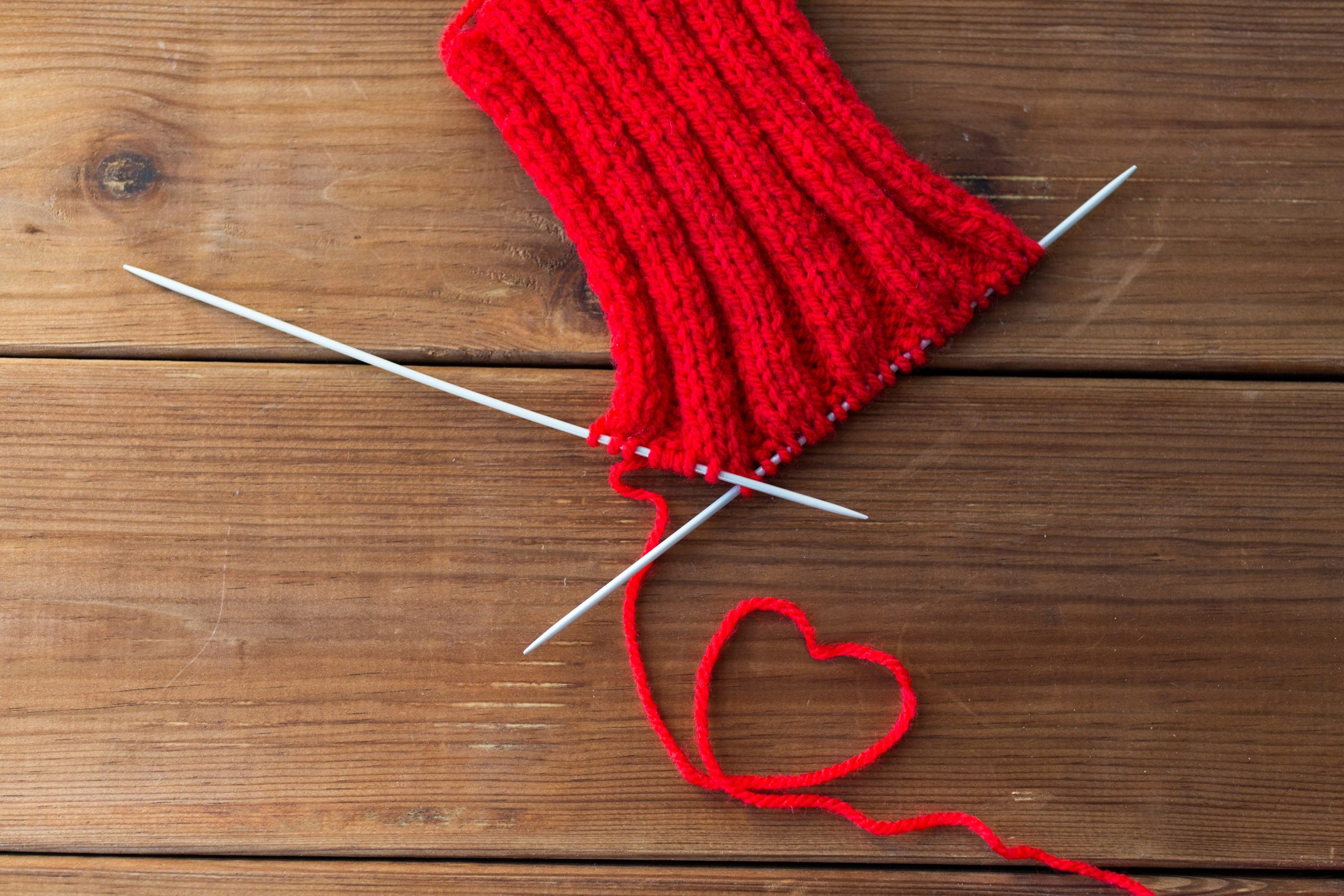 A red knitted sock with knitting needles on a wooden table.