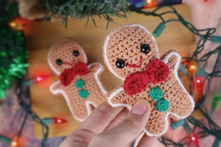 A person holding two crocheted gingerbread men.