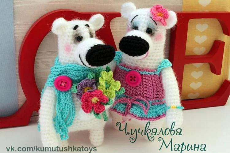 Two crocheted polar bears standing in front of a heart.