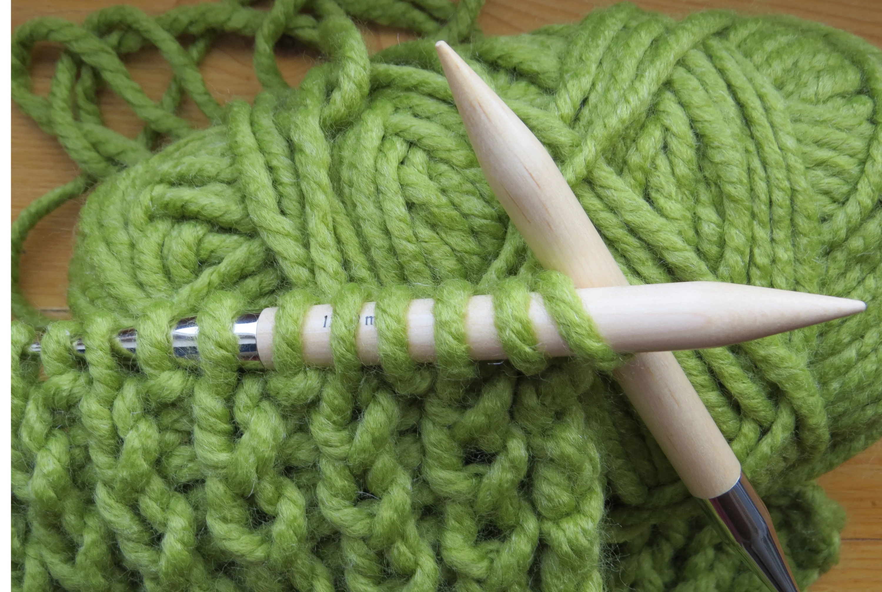 A pair of knitting needles demonstrating how to cast on with green yarn.