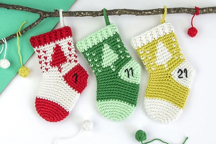 Three crocheted christmas stockings hanging on a branch.