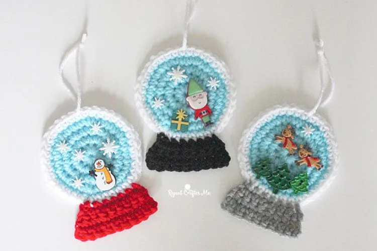 Three crocheted snow globe ornaments on a white surface.