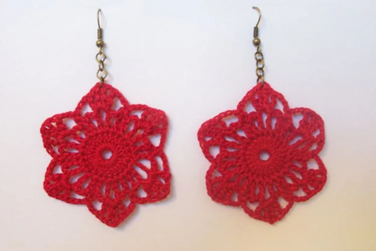 A pair of red crocheted flower earrings on a white surface.