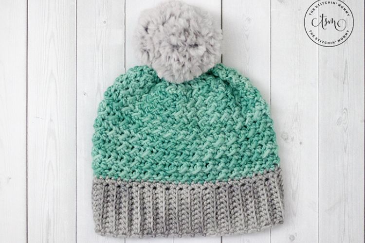 A green and gray knitted beanie with a pom pom.