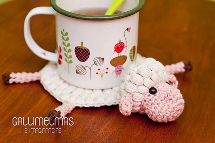 A crocheted sheep sits on top of a coffee cup.