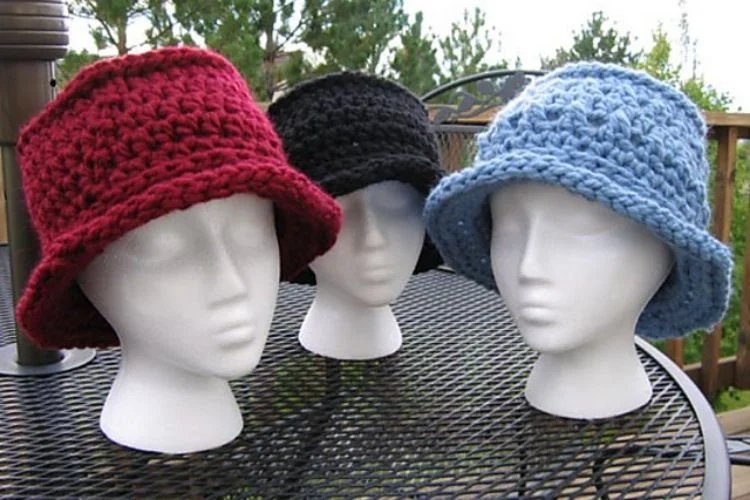 Three crocheted hats on mannequin heads.