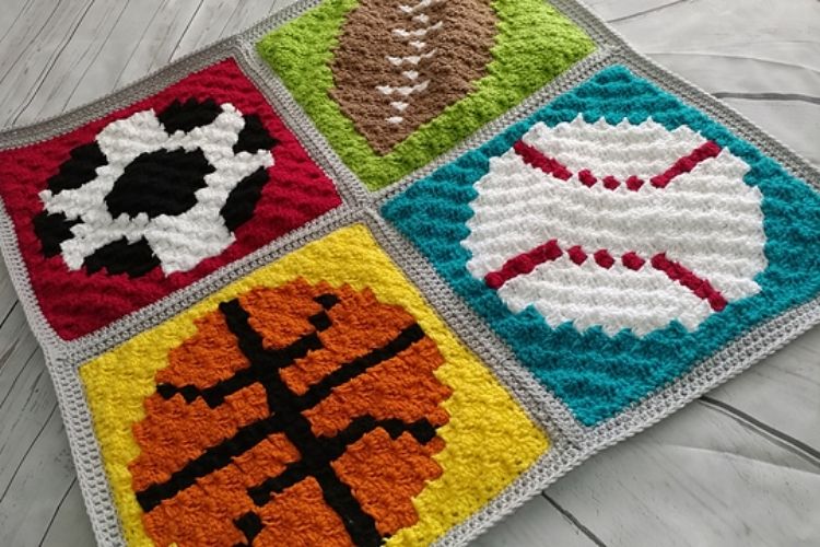 A crocheted afghan with different sports items on it.