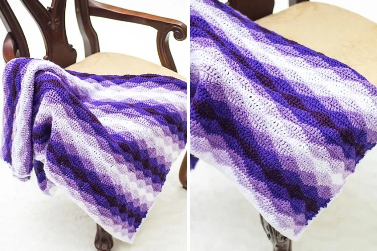 A purple and white crocheted afghan sitting on a chair.