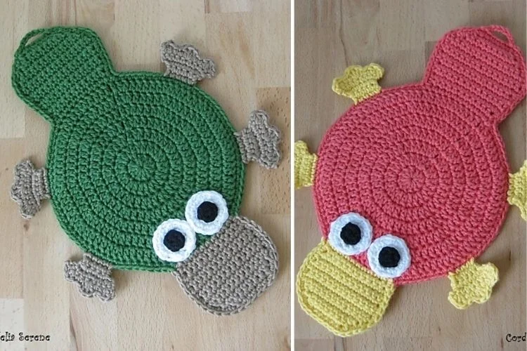 Two crocheted frogs on a wooden floor.