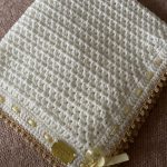 a crochet baby blanket with a cream body color and a yellow ribbon border