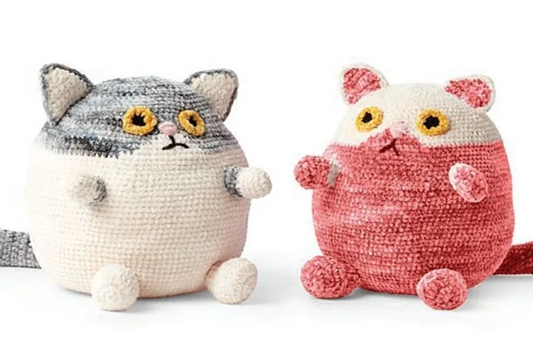 Two fat crocheted cats sitting next to each other.