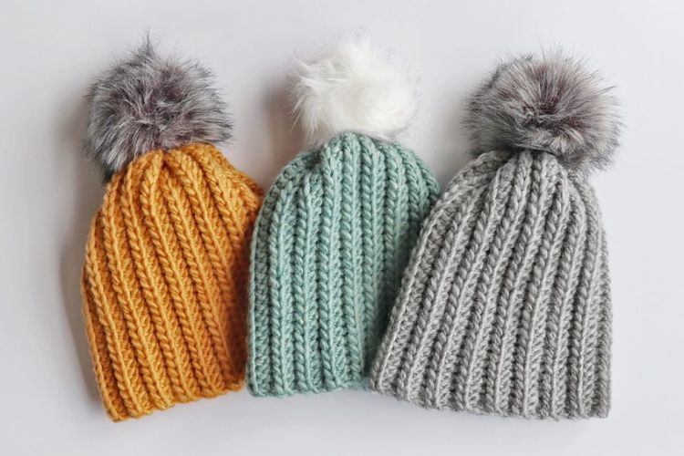 Three knitted beanie hats with pom poms.