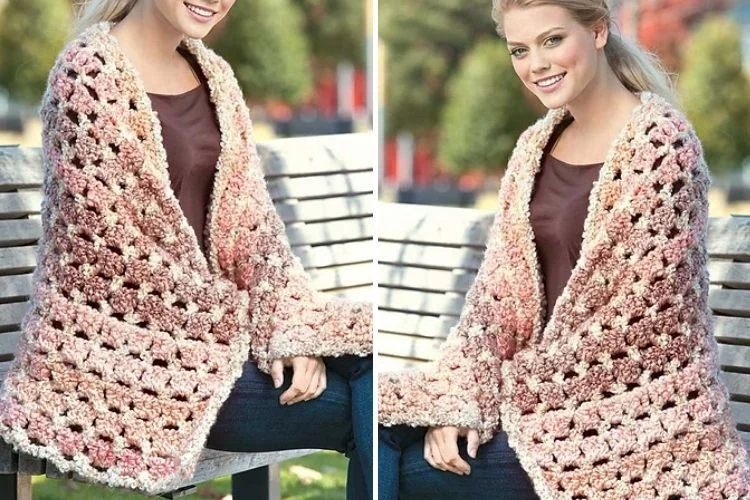 A woman is sitting on a bench wearing a soft and cozy crocheted shawl.