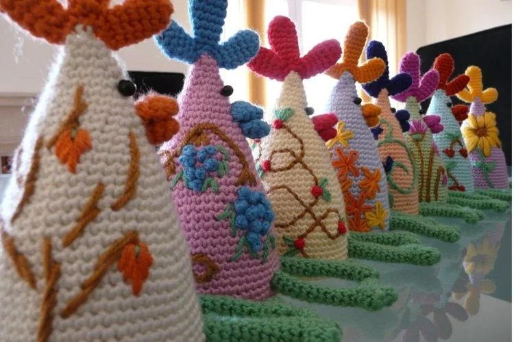 A row of crocheted rooster hats on a table.