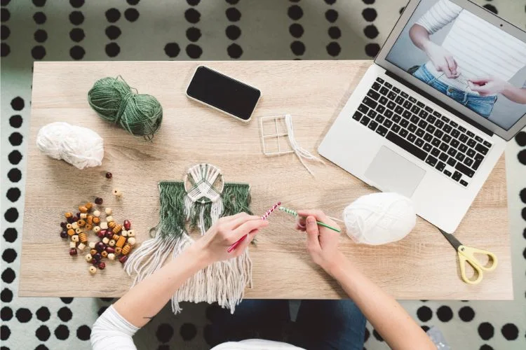 A woman working on a laptop with yarn and knitting needles.