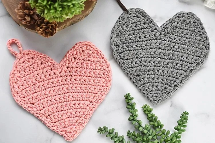 Two crocheted heart shaped potholders on a marble table.