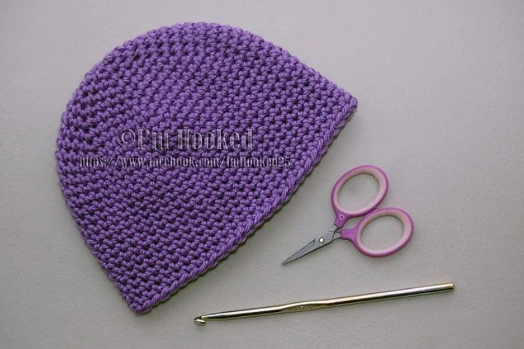 A purple crocheted hat with scissors and scissors.