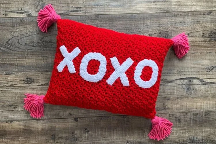 A red crochet pillow with the word xoxo on it.