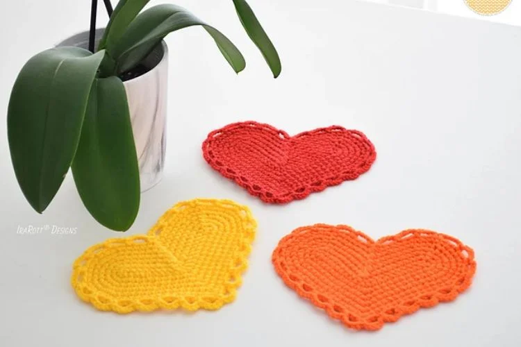 Three crocheted heart coasters next to a potted plant.