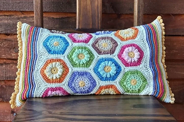 A colorful crocheted pillow on a wooden chair.