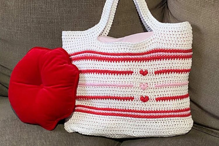 A crocheted tote bag with a red and white pillow.