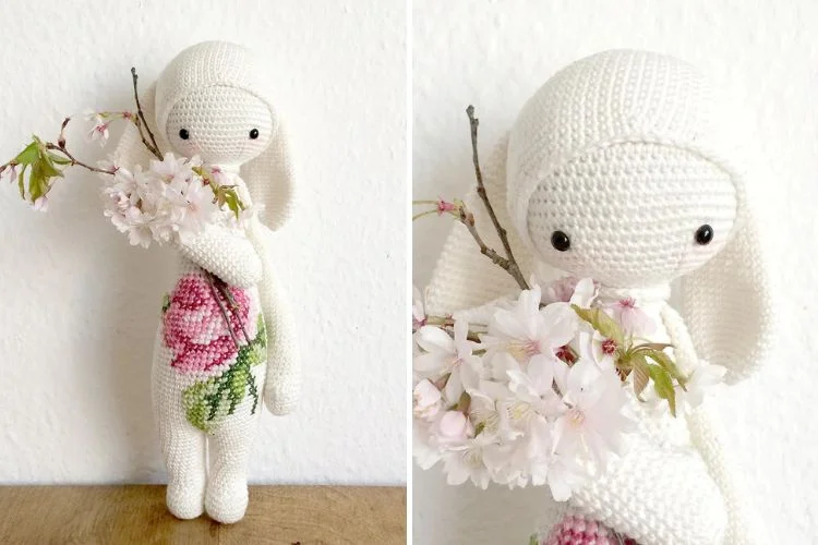 A white crocheted bunny holding a pink flower.