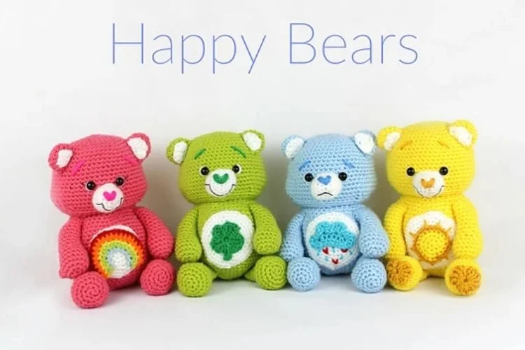 Four colorful crocheted teddy bears with happy expressions sitting in a row against a white background.