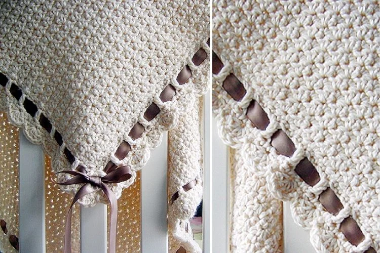 Crocheted baby blanket with ribbon detail draped over a crib railing.