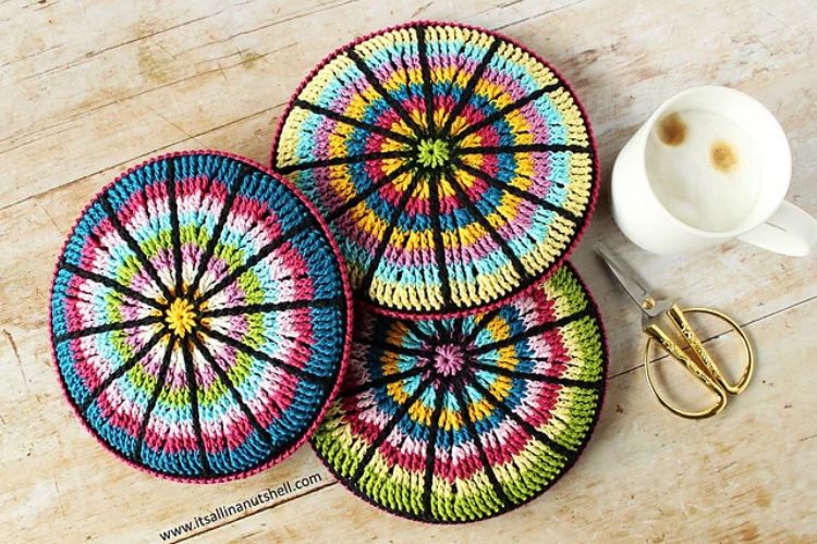 Four colorful crocheted coasters on a wooden table.