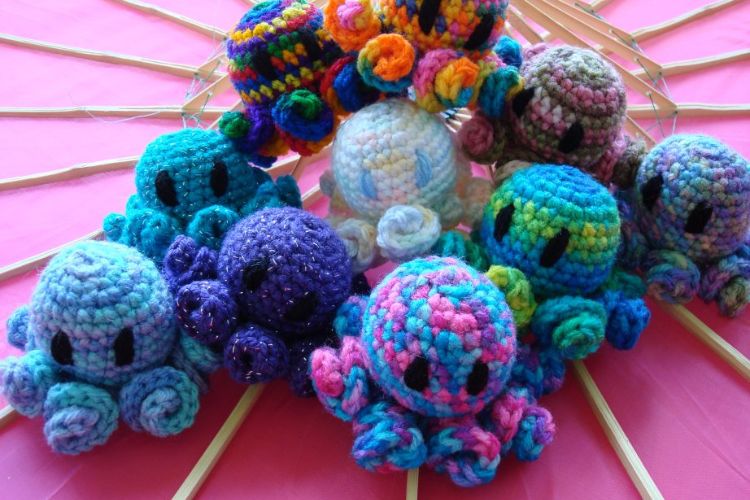 A collection of colorful crocheted octopus toys arranged on a pink surface.