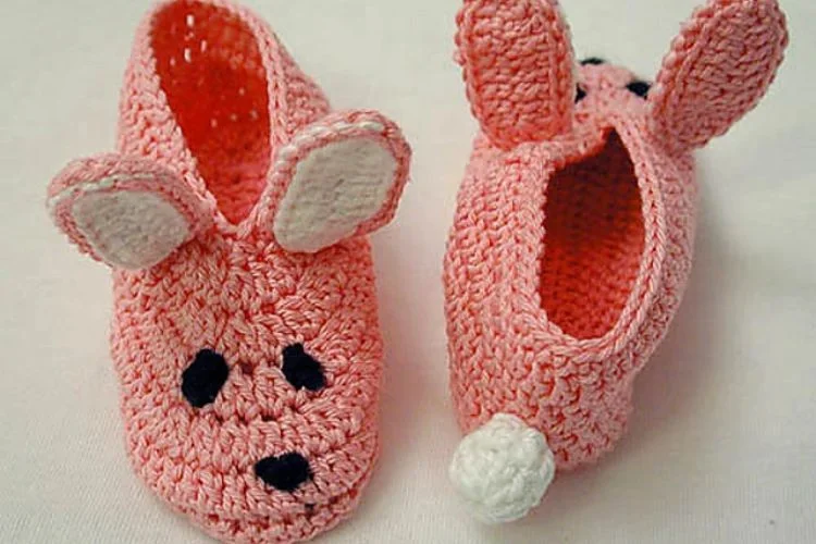 Pair of pink, bunny-shaped crochet baby slippers with facial features and ears.