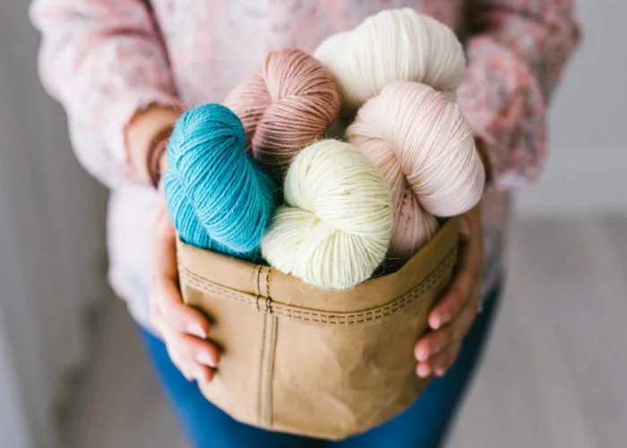 A woman holding a bag full of yarn and crochet tools.