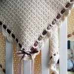 an elegant crochet baby blanket in a beige color adorned with a dark brown ribbon