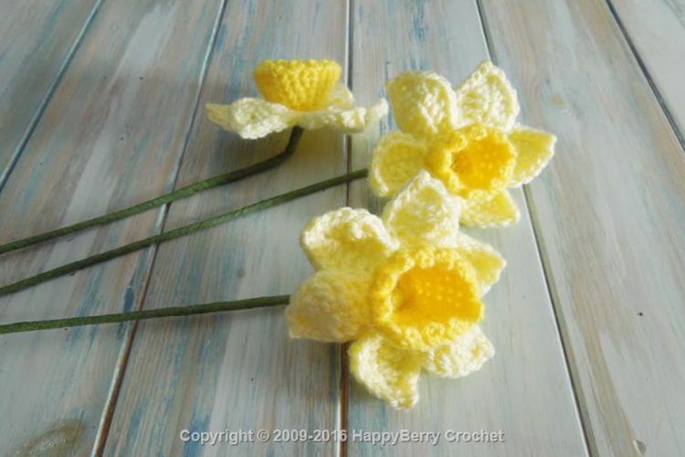 Three crocheted daffodils on a wooden table.