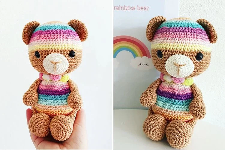 A colorful crocheted teddy bear with rainbow-striped clothing, displayed against a white background.